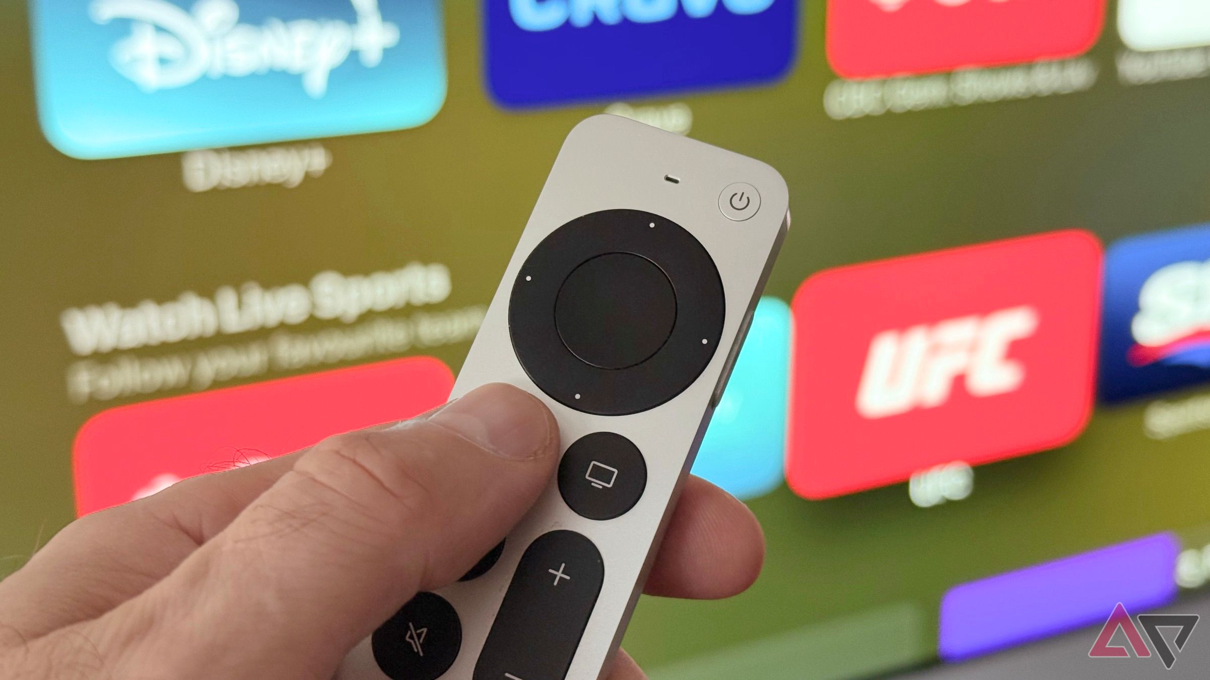 Hand holding the Siri Remote in front of an Apple TV screen