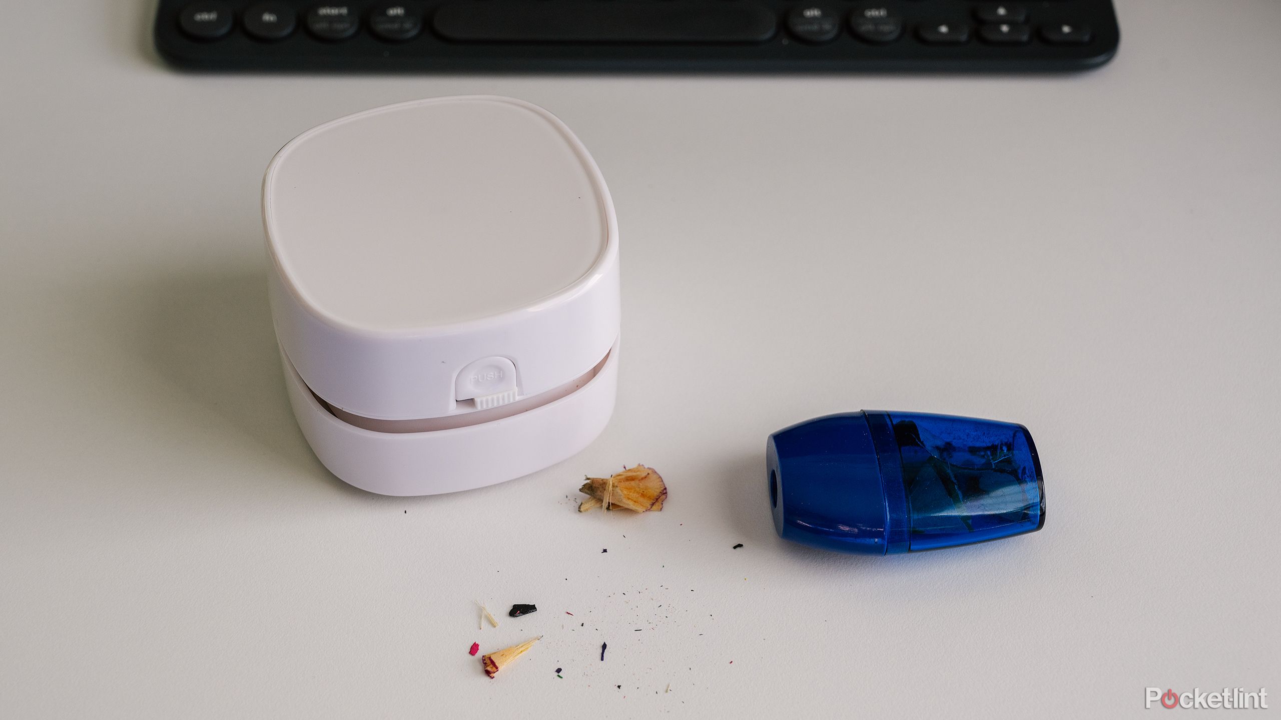 The white Odistar Desktop Vacuum Cleaner sits on a white desk next to a pencil sharpener and pencil shavings.