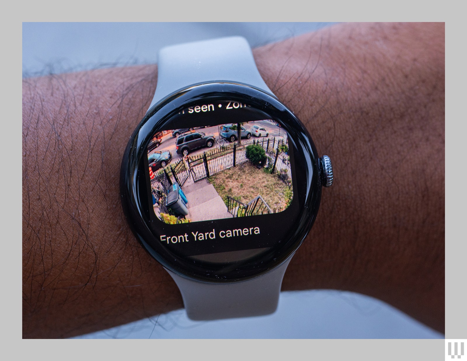 Person's wrist wearing a smart watch with the screen showing video footage of a front yard camera