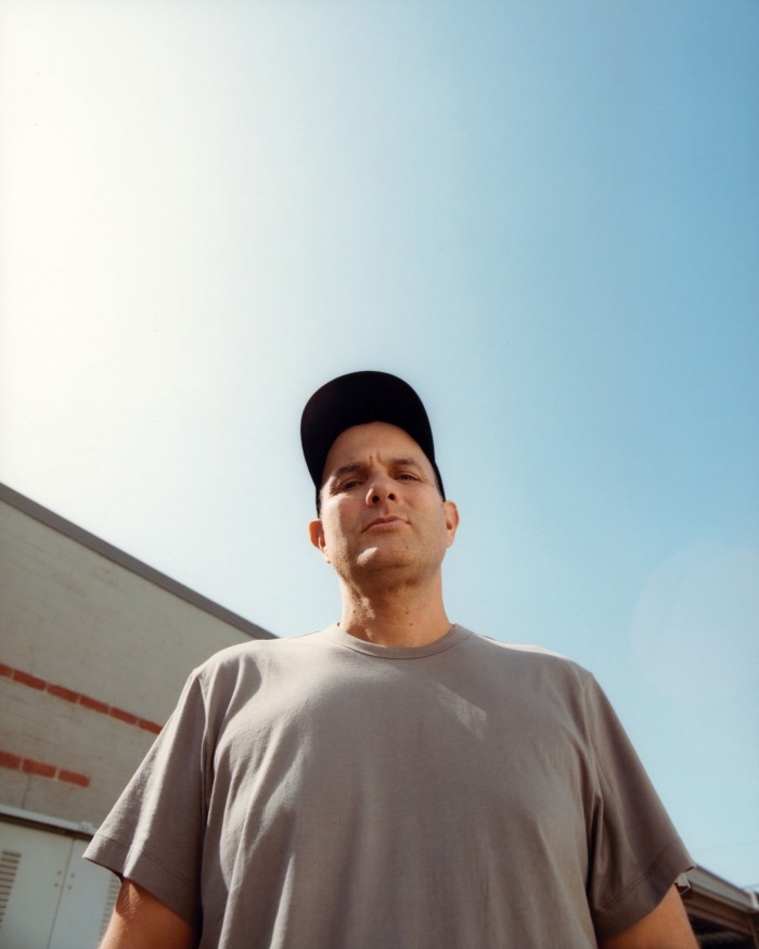 A fortysomething man wearing a grey T-shirt and and a black baseball cap stands beside a building under a blue Californian sky. He is John Janick, the CEO of the Interscope record label, whose signees include Billie Eilish and Olivia Rodrigo, pop’s biggest new stars of the past decade 