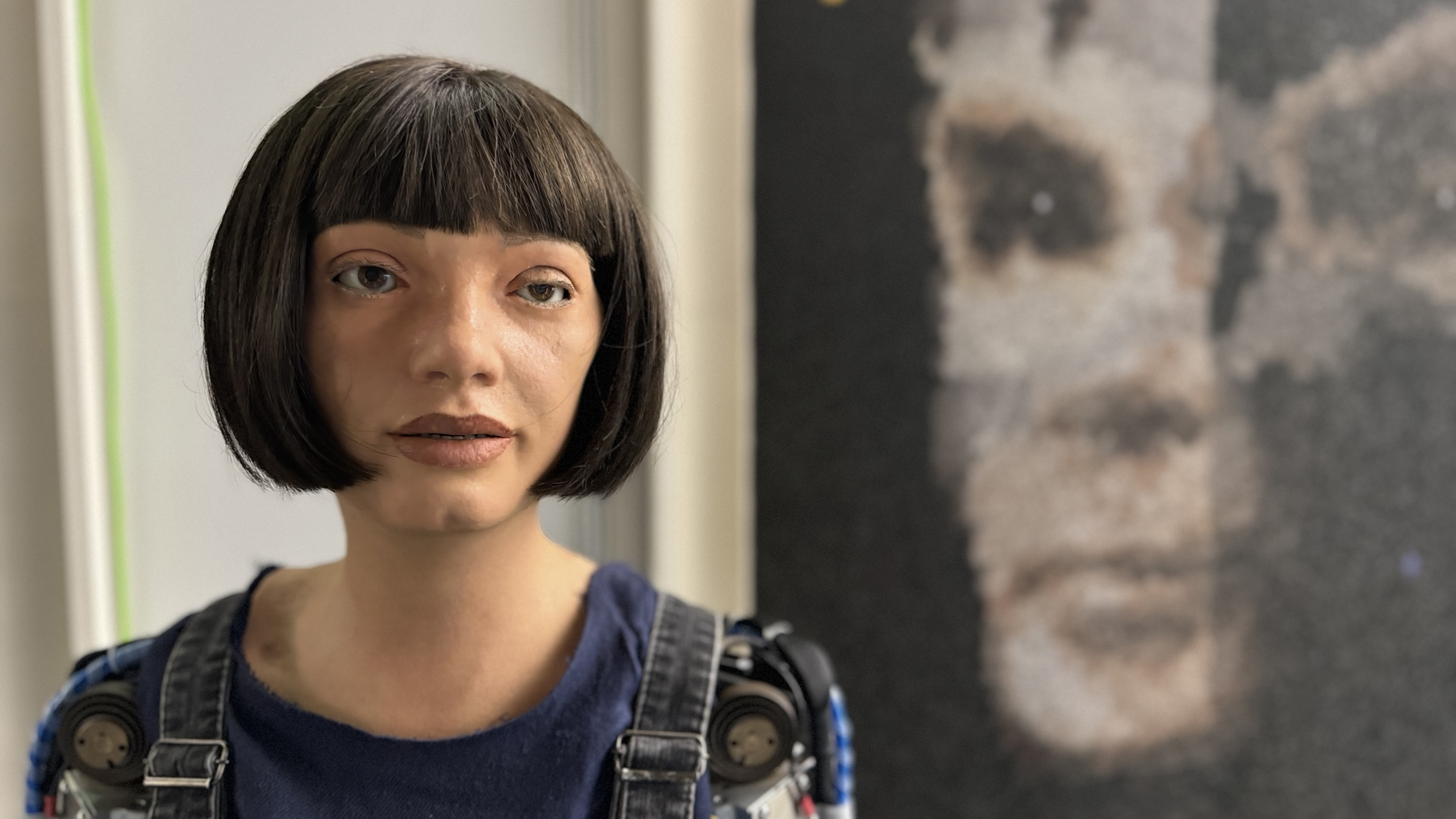 The Ai-Da robot standing in front of her 'AI God' painting on Alan Turing