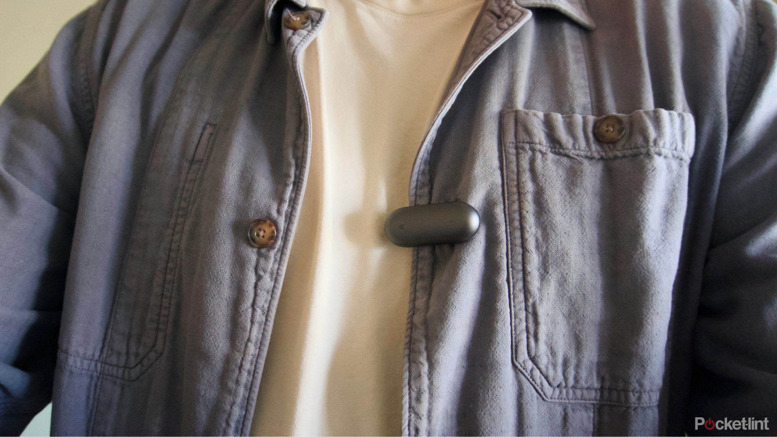 A blue jacket with a gray Plaud NotePin clipped to the side.