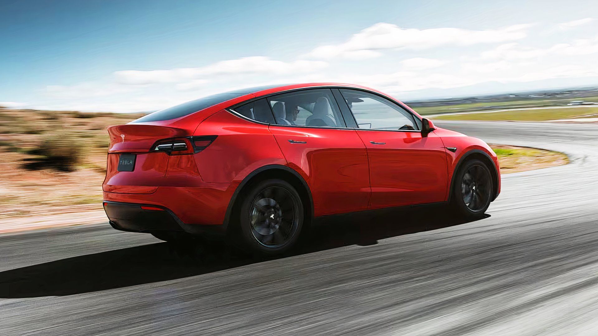 A red Tesla Model Y small electric SUV is driving on the road. 