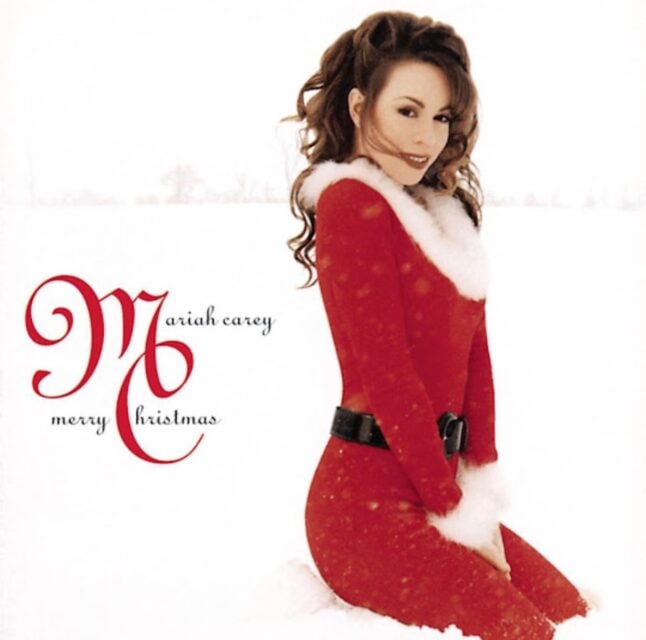 Smiling Mariah Carey in Santa outfit kneeling in the snow