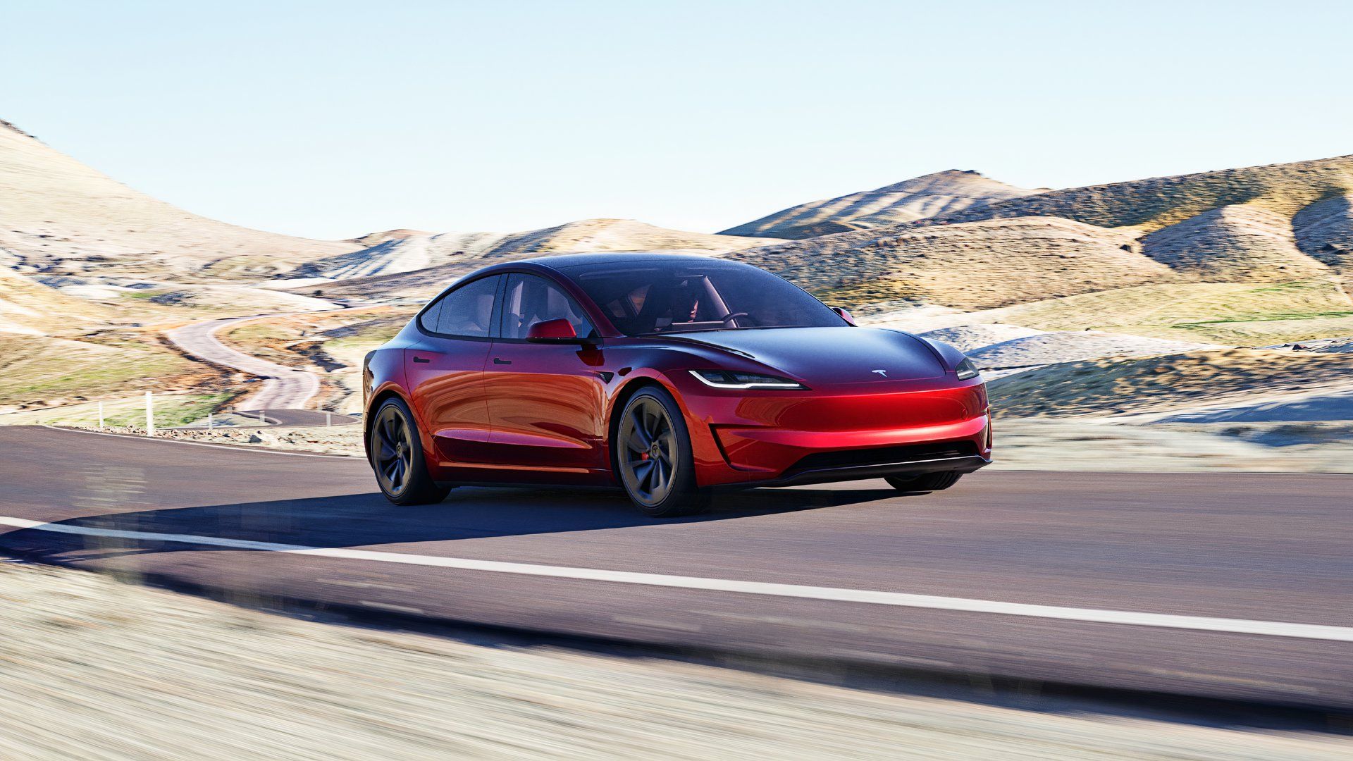 A red Tesla Model 3 electric sedan is driving on the road. 