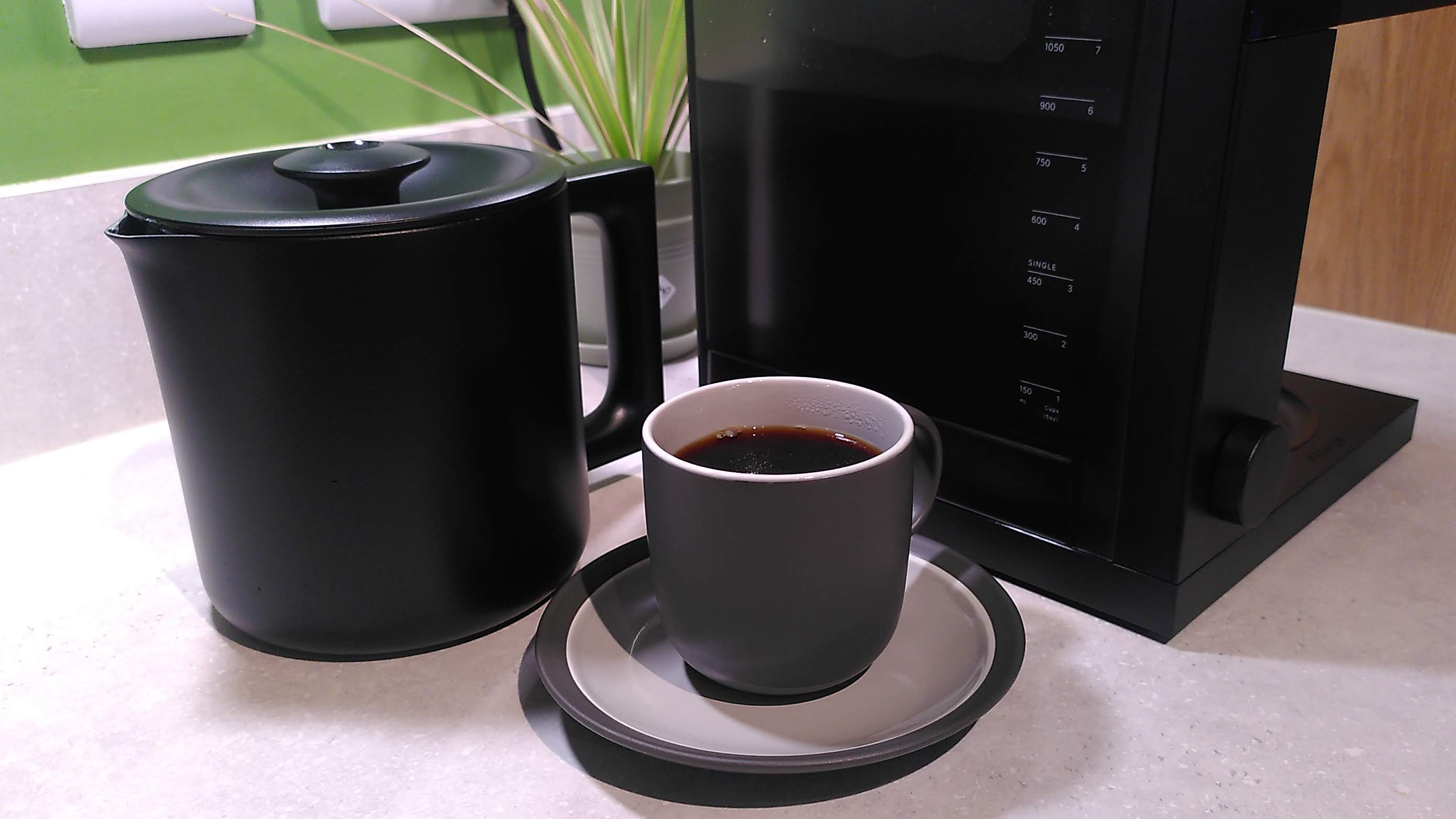 Fellow Aiden Precision Coffee Maker on counter with carafe removed, cup of coffee and small plant