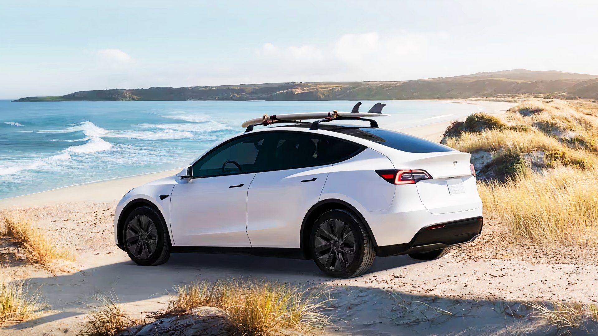 A white 2024 Tesla Model Y small electric SUV is parked on a sandy beach. 