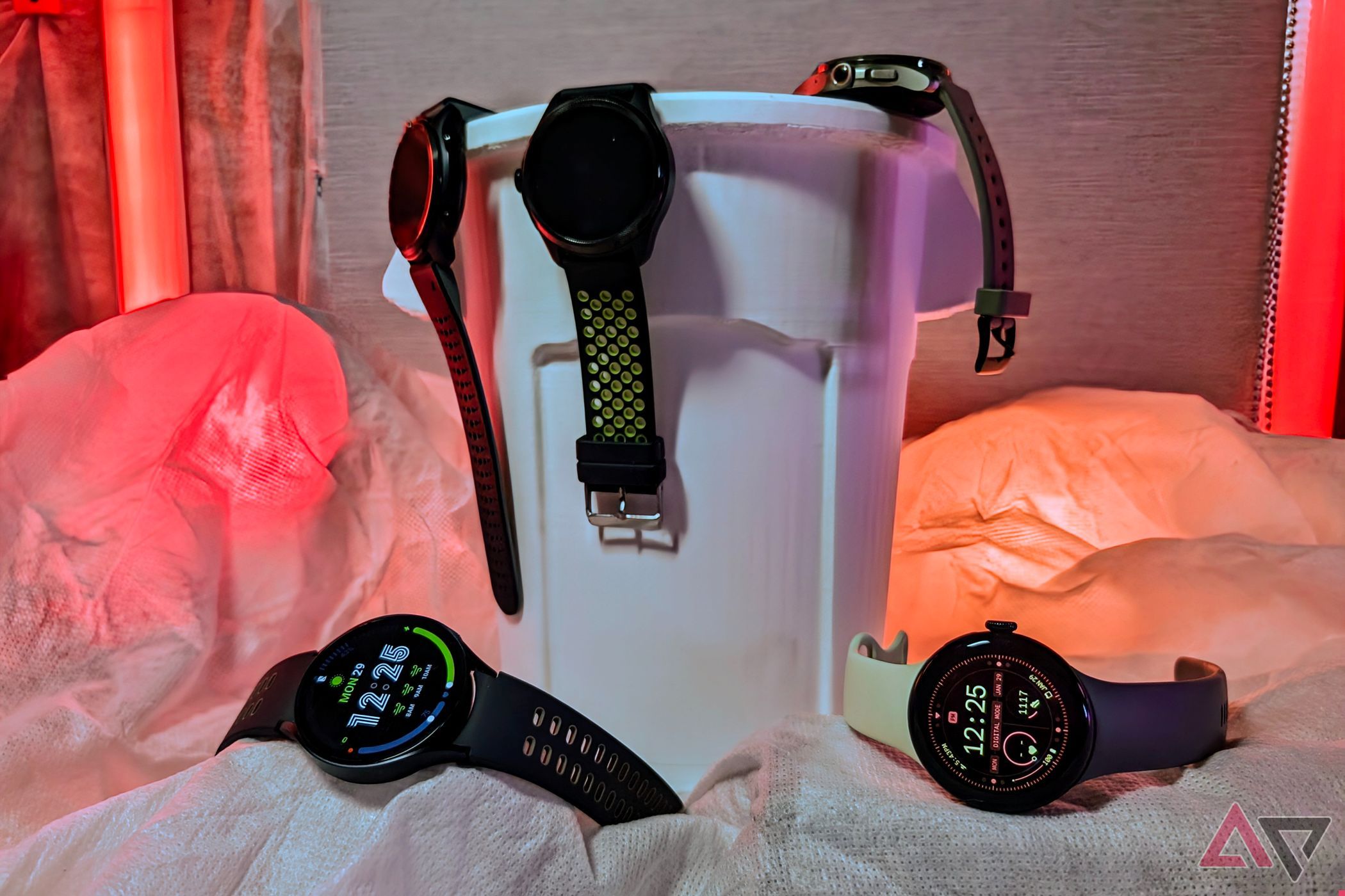 Samsung Galaxy Watch 6 and Pixel Watch 2 outside of a trash can with other Wear OS watches on the edge of it