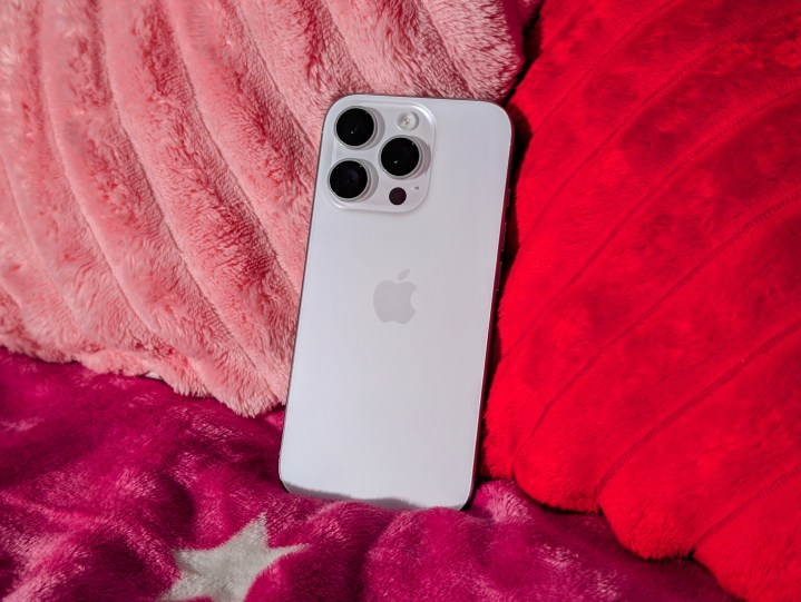 White Titanium iPhone 16 Pro sitting on blankets with heart pillows behind.