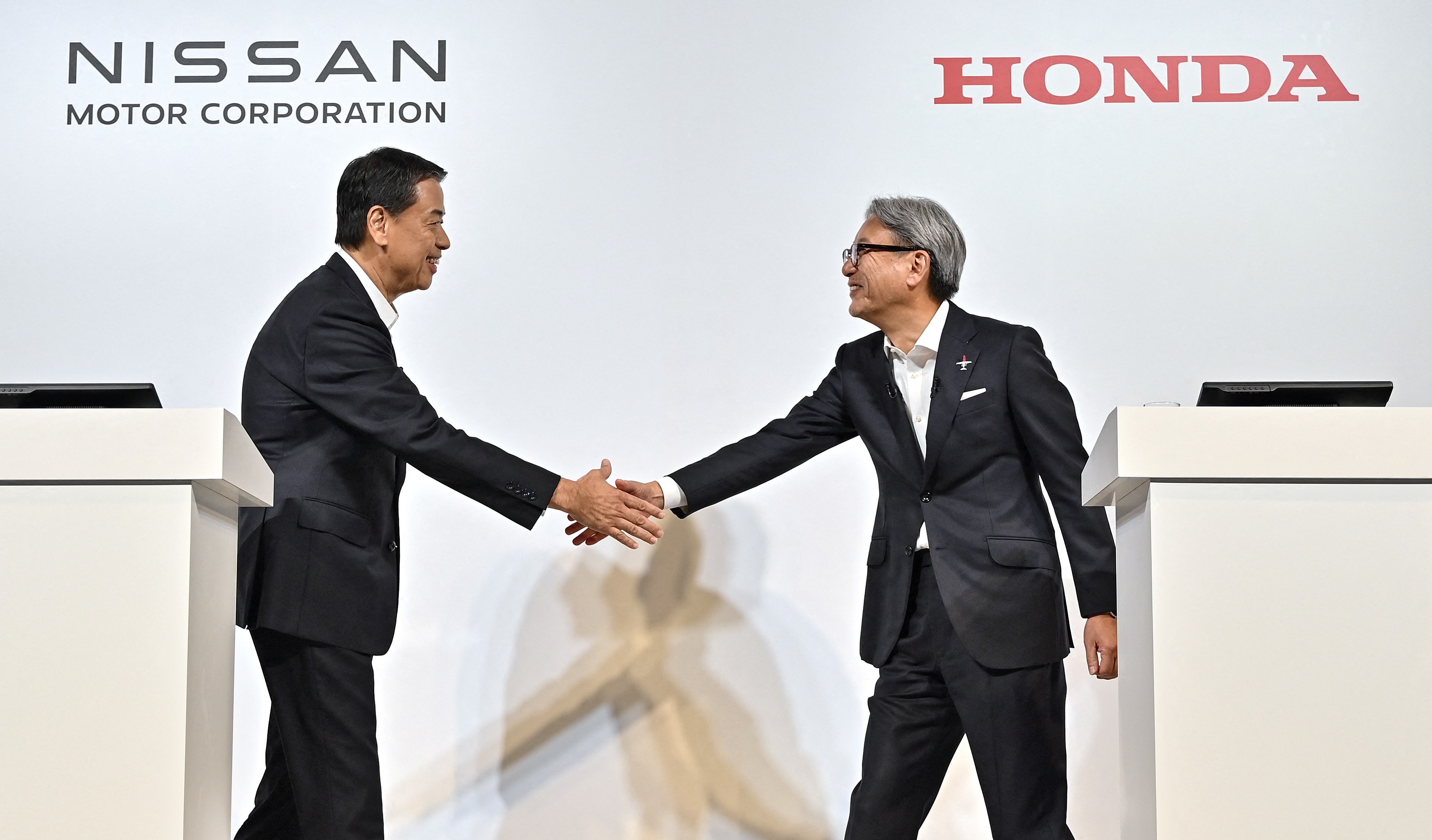 Nissan and Honda CEOs shaking hands at a press conference.