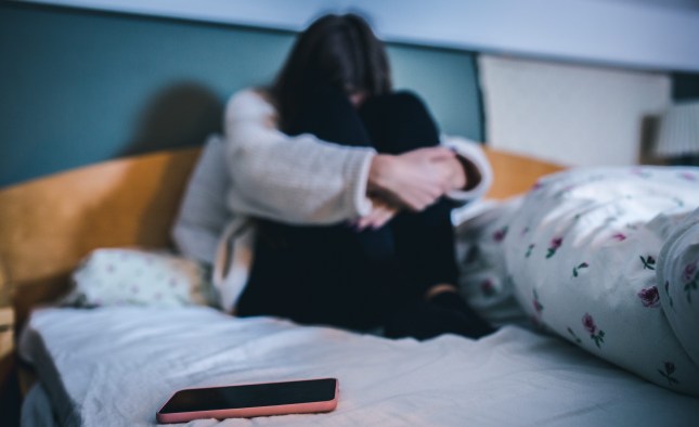 Sad teen with a phone in her bedroom