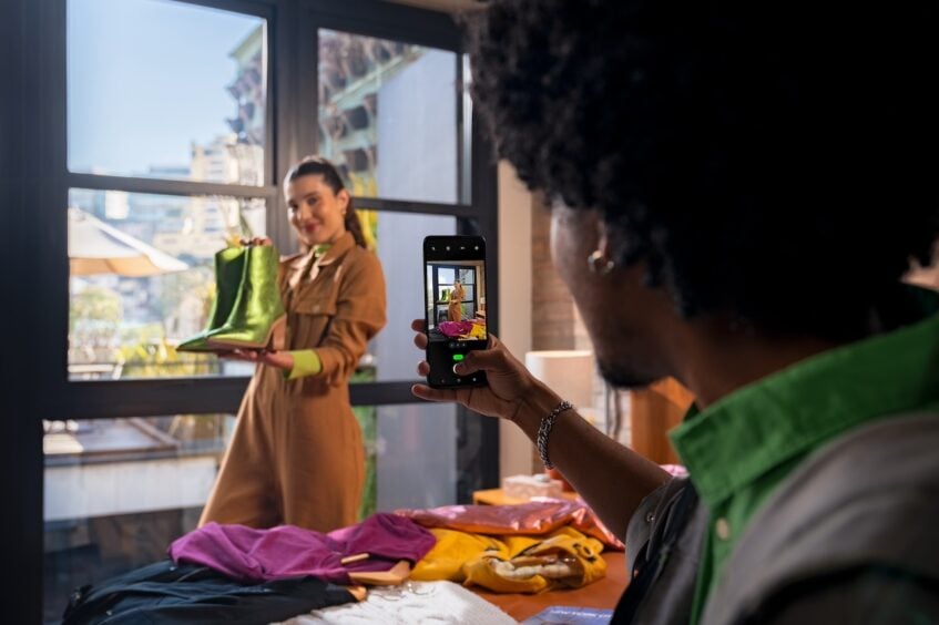 Man taking picture of smiling woman holding up green boots