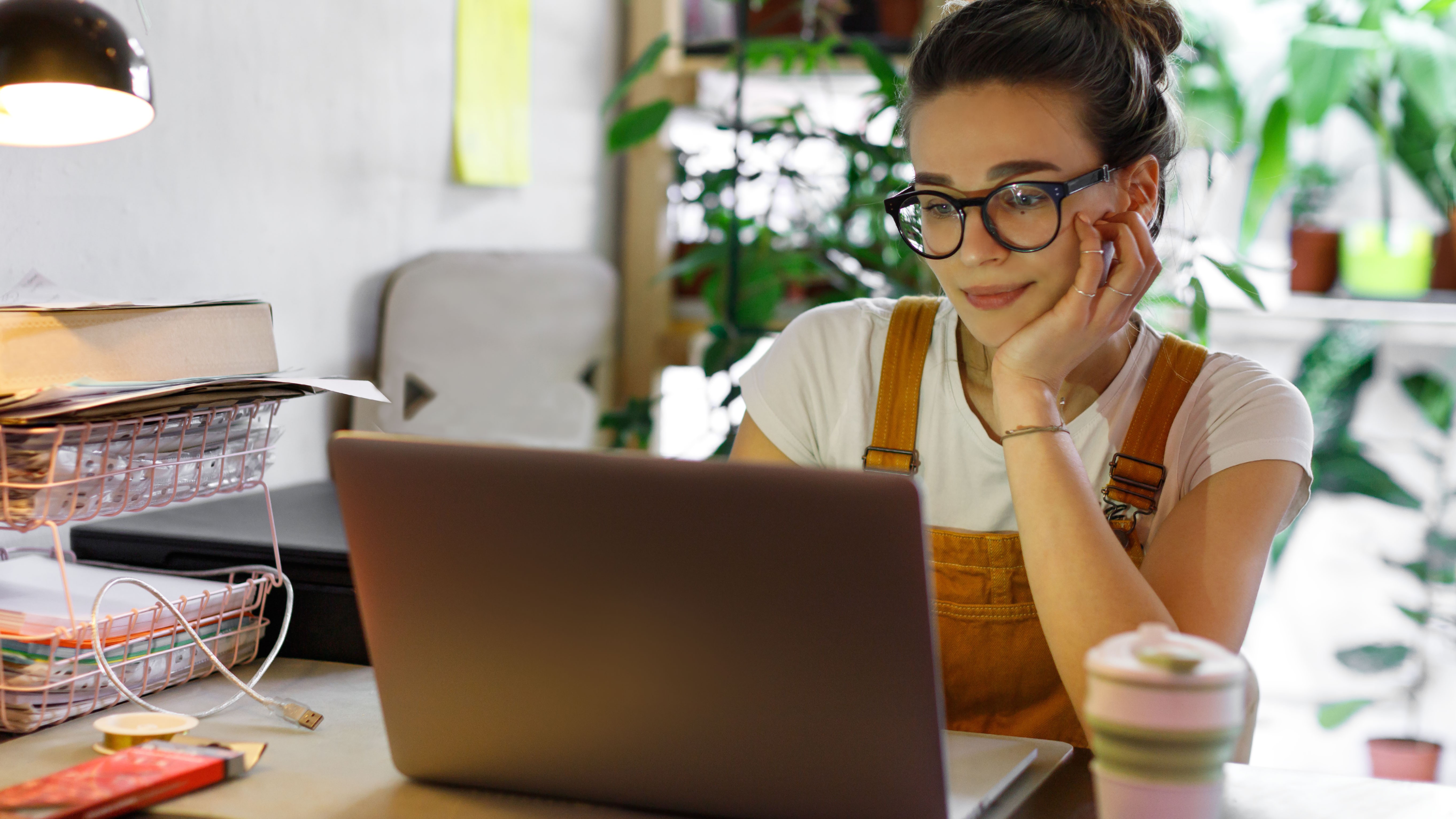 A woman sitting at a desk and using a MacBook, and there's a background of several indoor plants