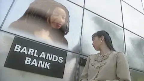 A woman at a future bank, speaking to a hologram with the sign Barlands Bank