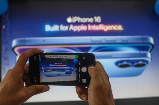 A man takes a picture of Apple's latest iPhone 16 billboard at Master Arts Shop in Srinagar, Jammu and Kashmir, on September 26, 2024. According to Apple Inc, the new iPhone 16 features Apple Intelligence, the new platform for artificial intelligence (AI) capability, larger display sizes, new creative capabilities, and an innovative camera. (Photo by Firdous Nazir/NurPhoto via Getty Images)