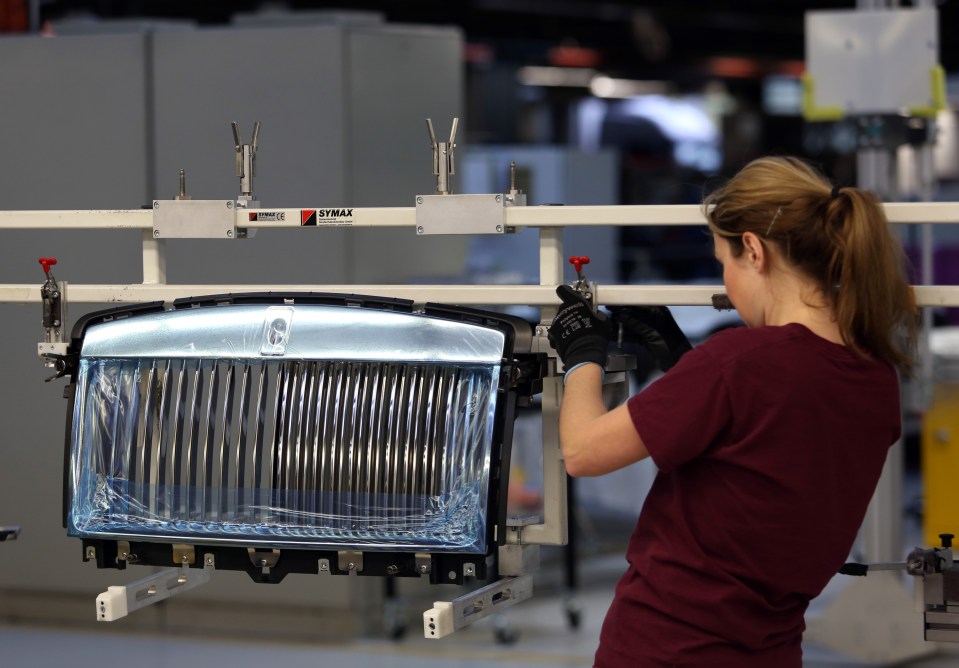 Factory worker attaching a Rolls Royce grill to a car frame.