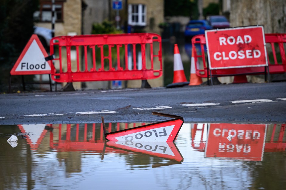 Flooded road with "Road Closed" and damaged "Flood" signs.