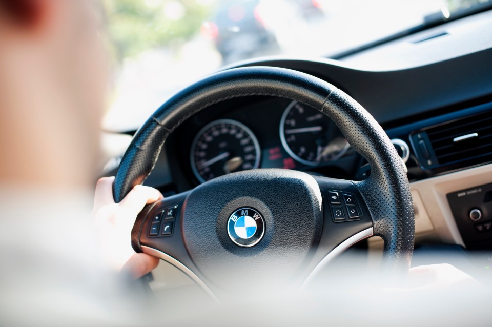 Close-up of a person's hands gripping the steering wheel of a BMW.