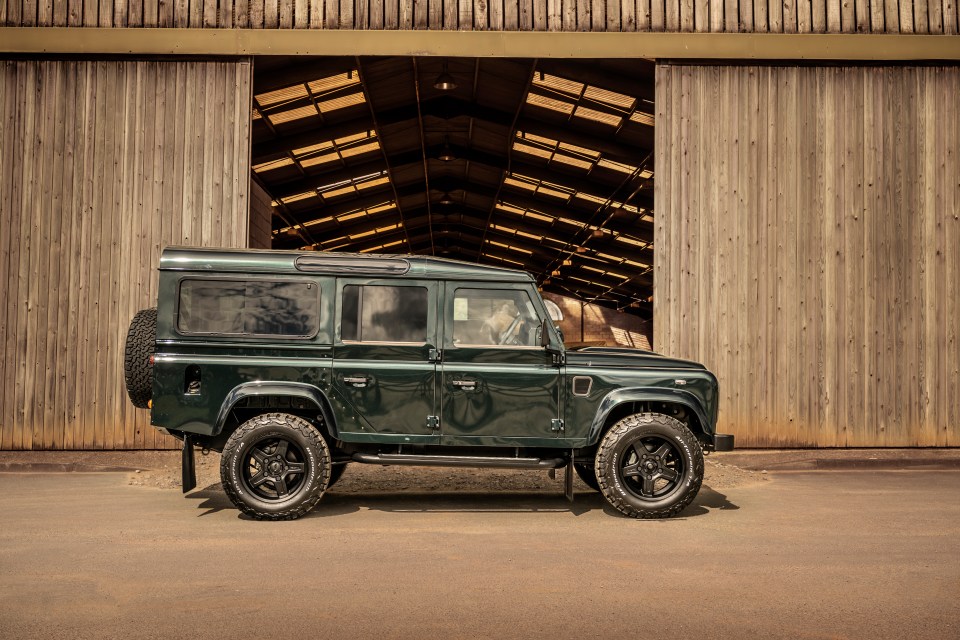 Dark green Land Rover Defender parked outside a barn.