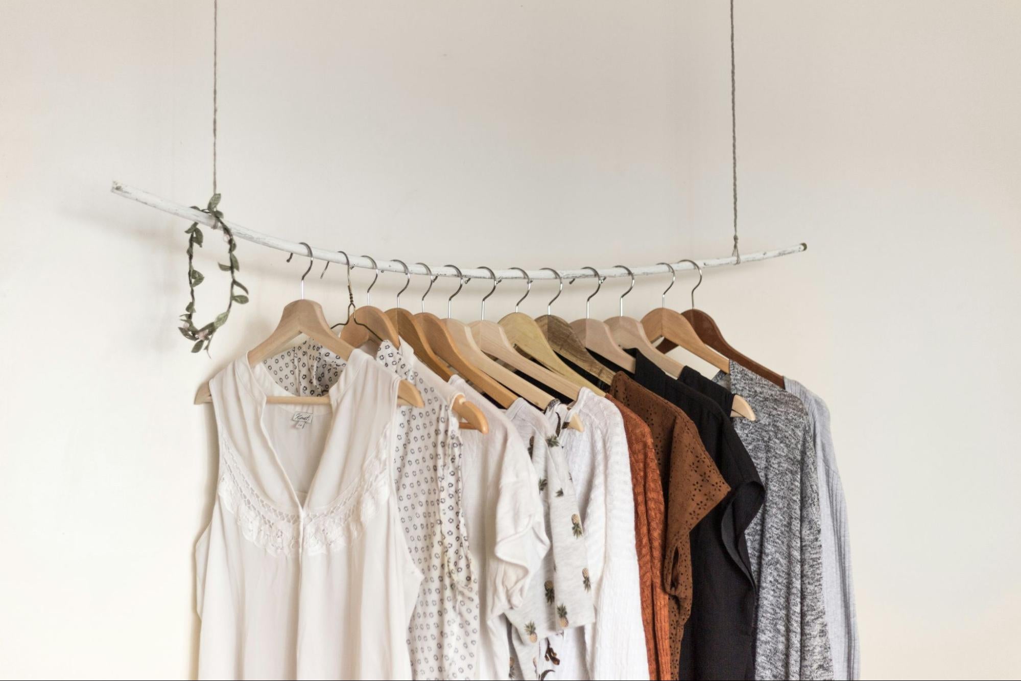 Assorted clothes on wooden hangers against a white background.