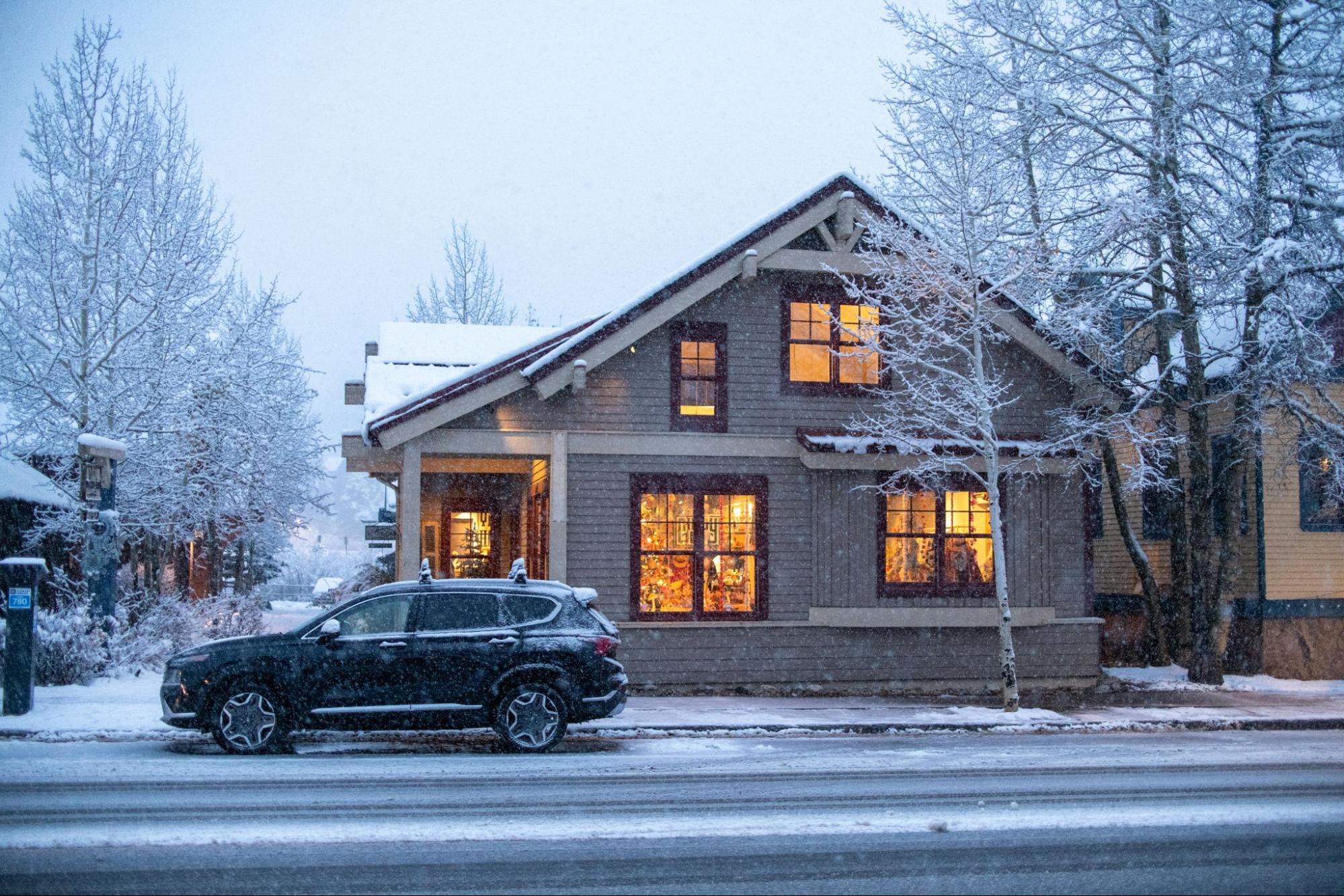 A car parked in front of a cozy house on a snowy day.