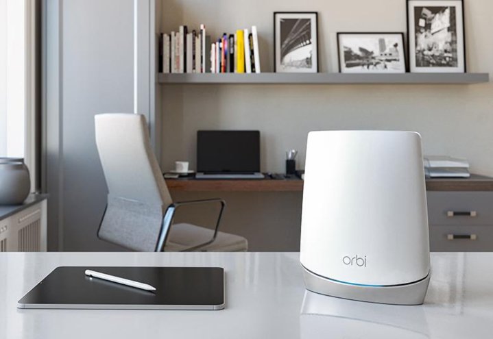 Netgear's Orbi CBR750 sits on a table beside an iPad, with a laptop is in the background.