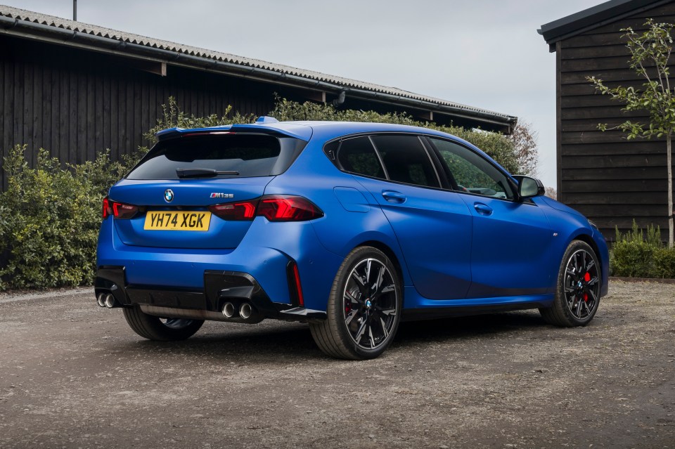 Rear view of a blue BMW M135i parked in a gravel driveway.