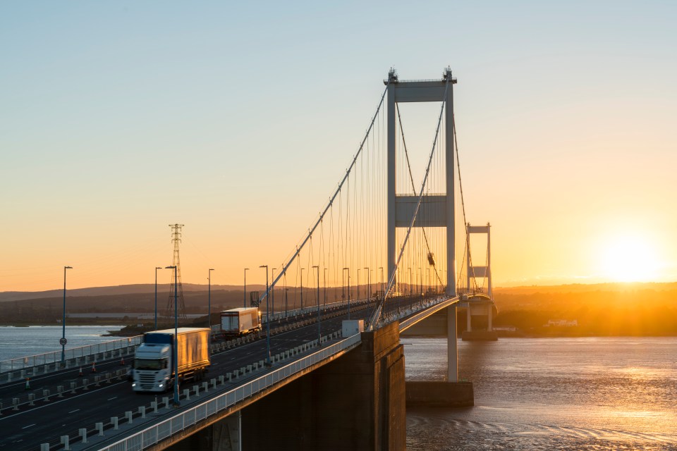 A suspension bridge at sunset with a truck driving across it.