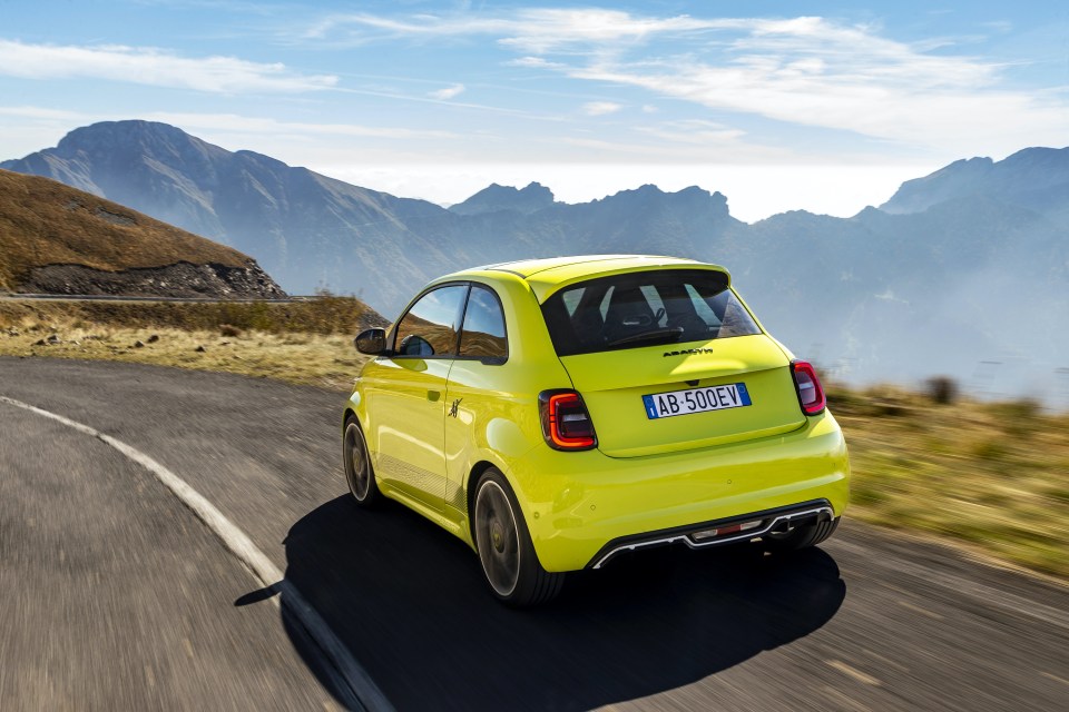 Yellow Abarth 500e electric car driving on a mountain road.