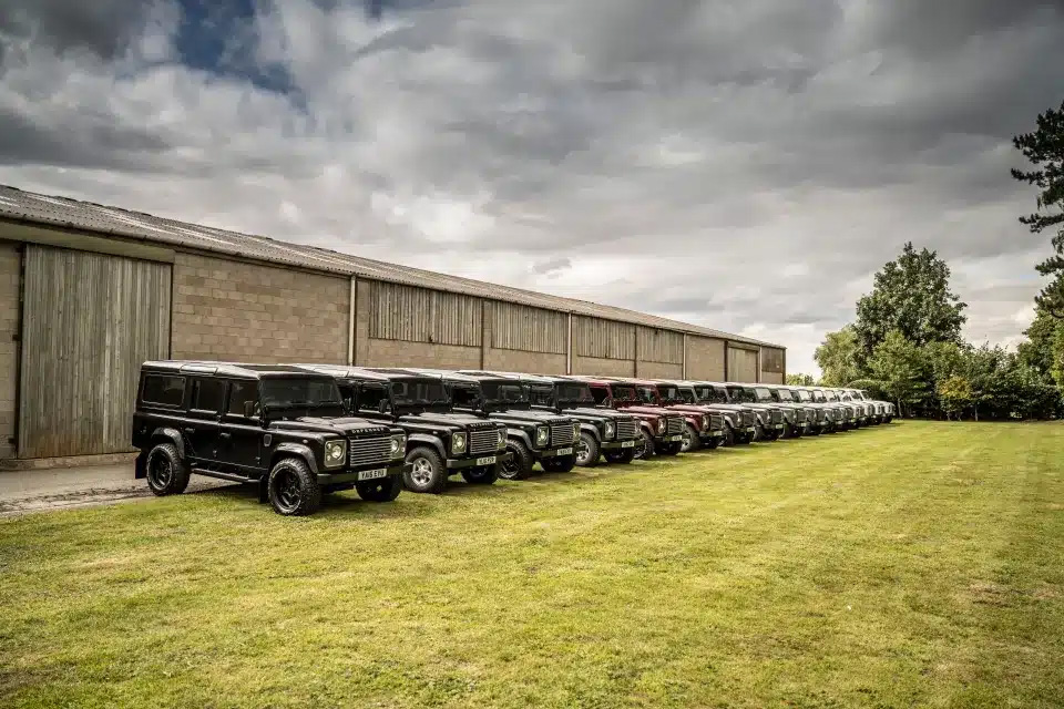 Row of Land Rover Defenders parked outside a barn.