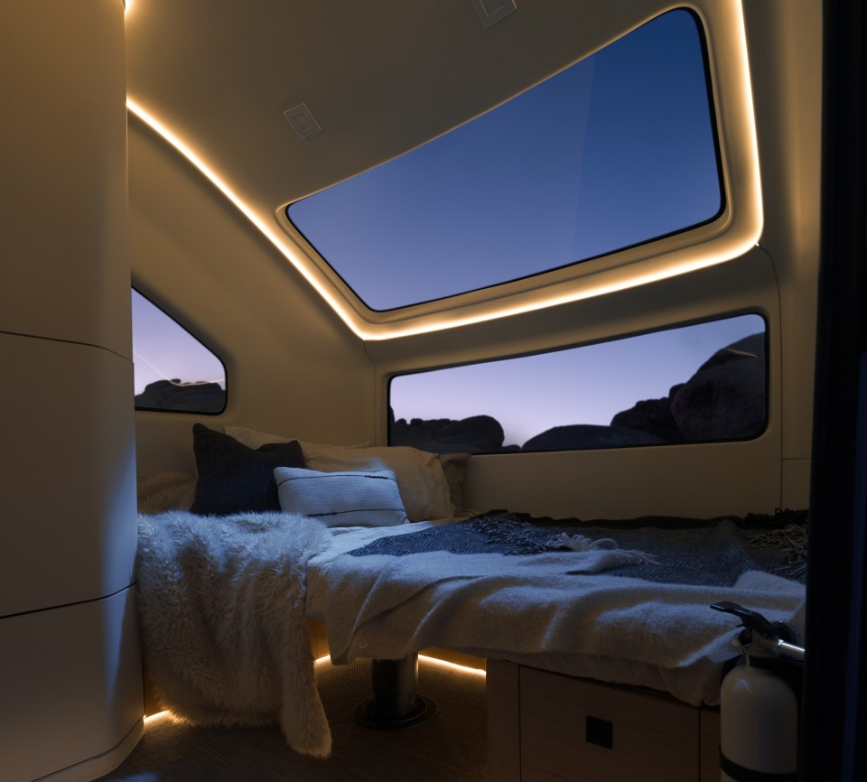 Interior of an electric caravan at night, showing a bed with blankets and pillows.