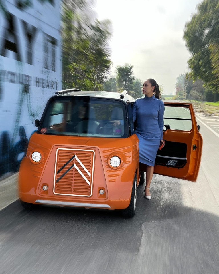 Woman standing by an orange Citroën Ami.