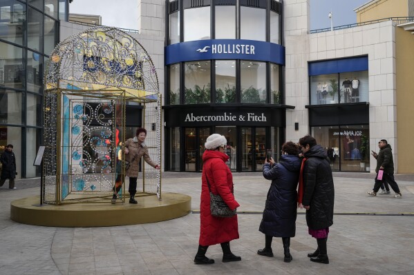 Women take a picture with a decoration on display near an American fashion boutiques at an outdoor shopping mall in Beijing, Tuesday, Feb. 4, 2025. (AP Photo/Andy Wong)