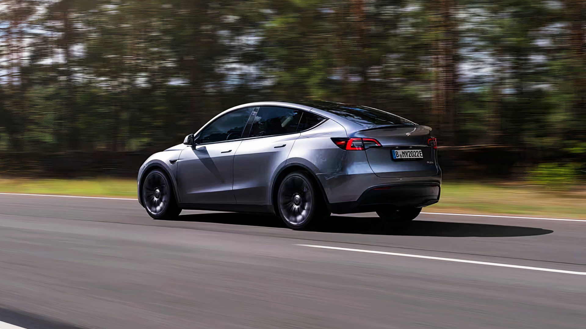 A gray Tesla Model Y is driving on the road. 