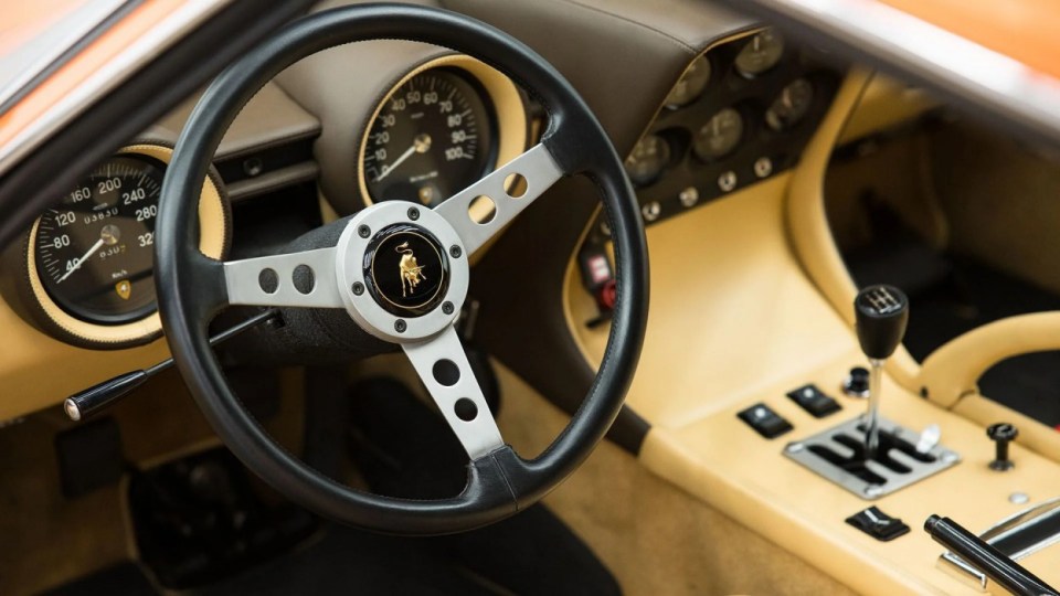 The steering wheel, USA, YOU COULD OWN this rare 1971 Lamborghini Miura P400 SV for ¿4M at auction. Images show this stunning Lamborghini finished in a unique combination of Arancio Miura or Miura Orange paintwork over a retro Goby sand interior. The Miura SV is one of only about 150 of its kind ever built, making it an incredibly rare find for collectors. One of the first 25 cars built, this Miura features early design elements such as the absence of ¿ears¿ on the wheel spinners and bodywork slats with rounded edges, marking it as a distinctive early example of the SV. This particular model is further distinguished by its European specification, devoid of U.S. specific safety features like side repeaters, and it is equipped with a matching numbers chassis and engine. Chassis No. 4854 and Engine No. 30647 trace a fascinating history, beginning with its delivery in July 1971 to Hubert Hahne, a renowned German racing driver and Lamborghini agent. This Miura has an illustrious provenance, having been part of the Rosso Bianco Collection for over three decades, where it shared space with some of the finest sports cars in the world. The car¿s remarkable journey included ownership by notable figures, such as former racing driver Peter Kaus. The meticulous nut-and-bolt restoration took place between 2014 and 2016 and cost close to ¿250K. It was carried out by award-winning Modenese Lamborghini experts, including Carrozzeria Cremonini handling the bodywork and Top Motors working on the mechanicals, alongside other industry leaders. The 1971 Lamborghini Miura P400 SV is set to be auctioned at The Amelia Auction in 2025. ¿The car's striking original colours were briefly altered, as records show it was painted in Luci del Bosco Green before its first private owner, but it has since been restored to its original Miura Orange exterior. "By the early 1980s, the car was acquired by former racing driver and renowned collector Peter Kaus," who added it to his world-famous collection. ¿During this time, the car showed around 60,000 kilometers, believed to be original, before it was sold and carefully restored. "Any Miura SV is a rare motorcar. ¿But an SV such as this, restored to its original and correct specification by the very best craftsmen in Modena, is truly a rare opportunity." ENDS