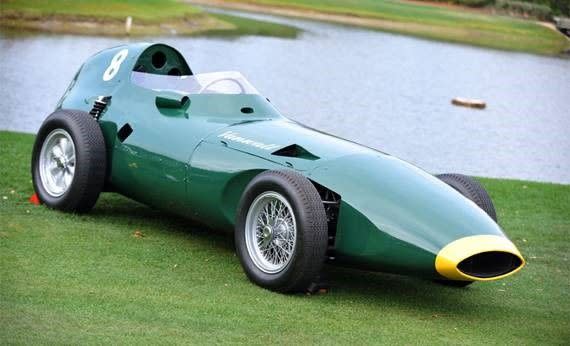 classic green racing car with yellow accents parked on grass near a body of water