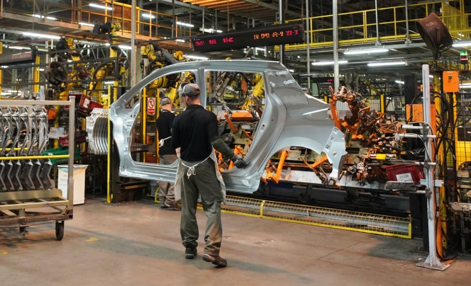 Factory workers assembling a car body using robots.