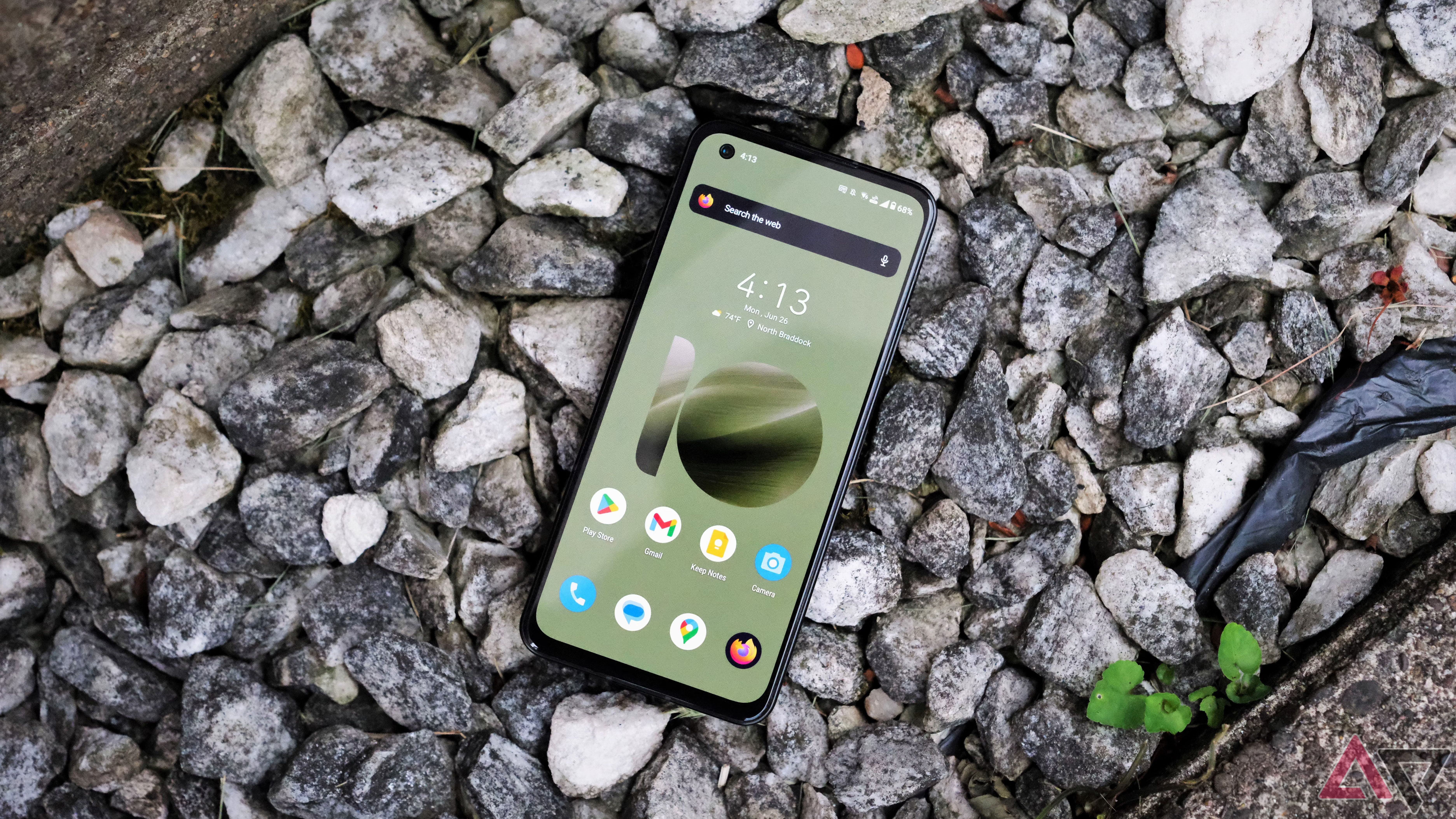 A smartphone with a green display rests on rocks.