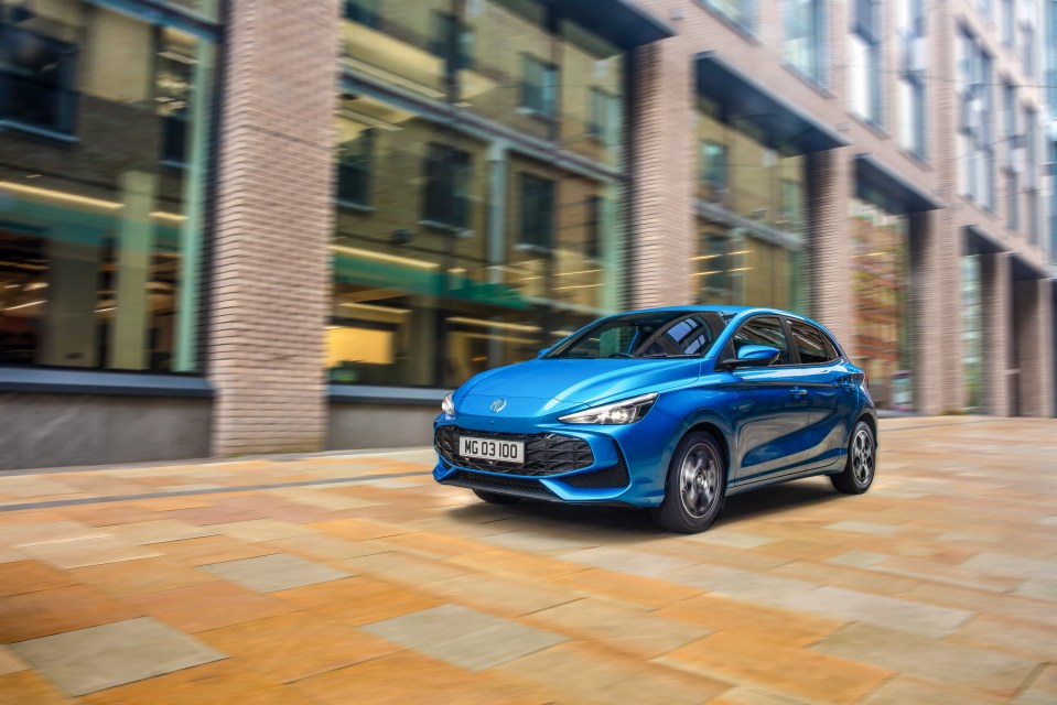 Blue MG car driving on city street.