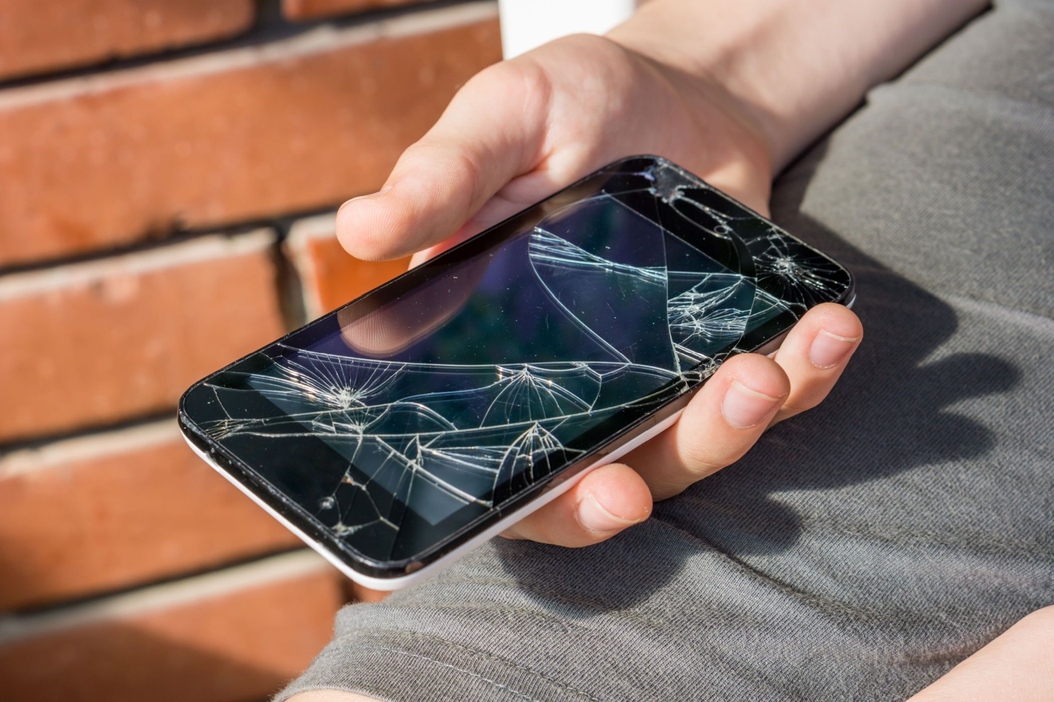 Close-up of a boy's hand looking at his still working phone with a broken screen.