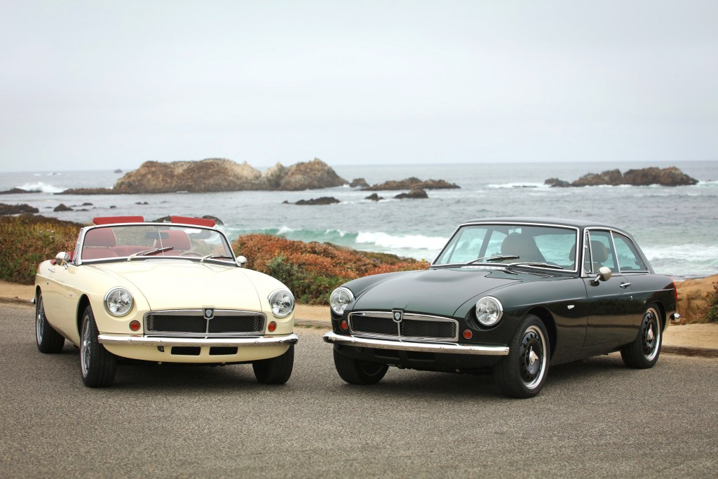 Two classic 1960s style British cars, one black and one off-white, parked in front of the ocean.