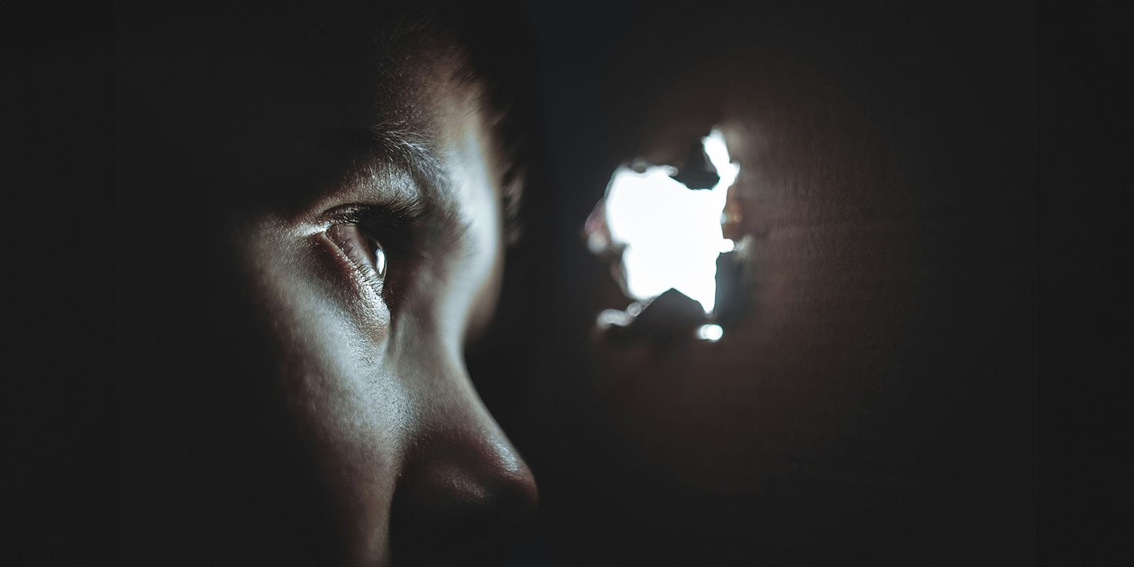 Apple currently only able to detect Pegasus spyware in half of infected iPhones | Close-up of man looking through a spy-hole in a wall