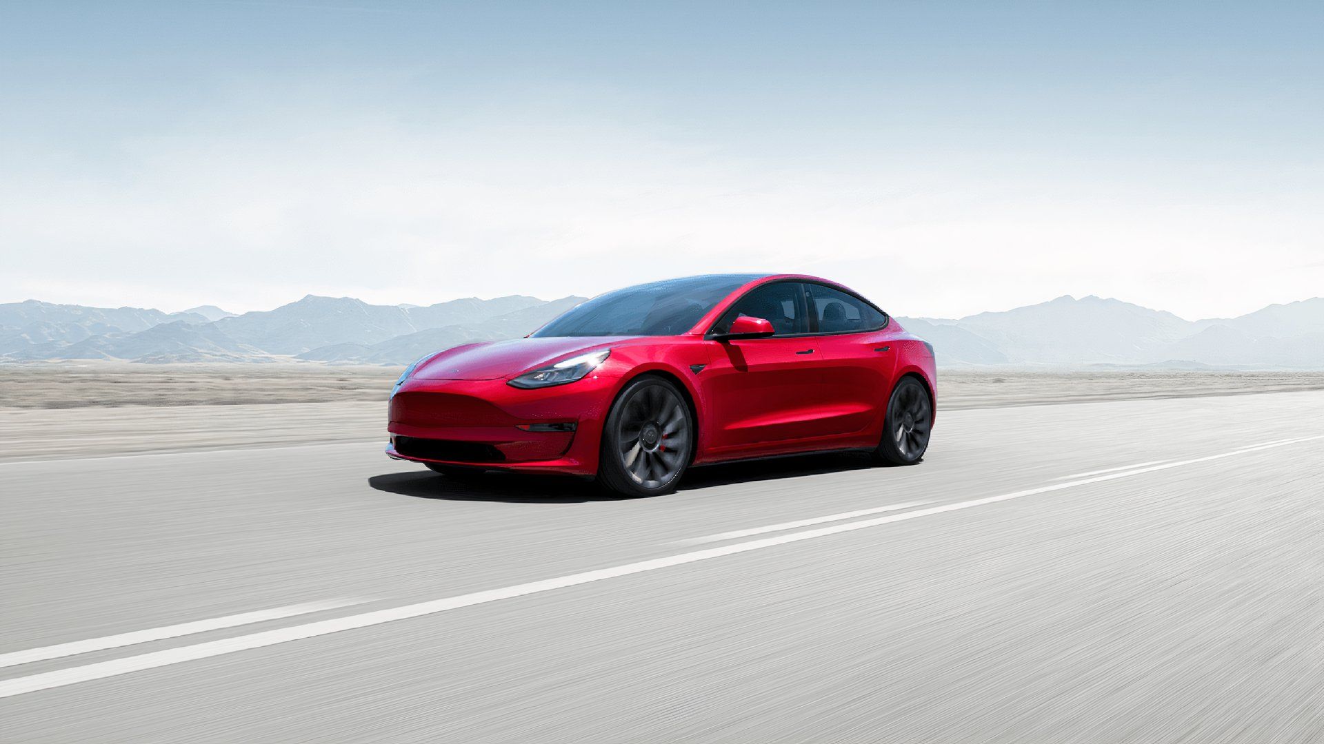 A red 2021 Tesla Model Y small electric SUV is driving. 