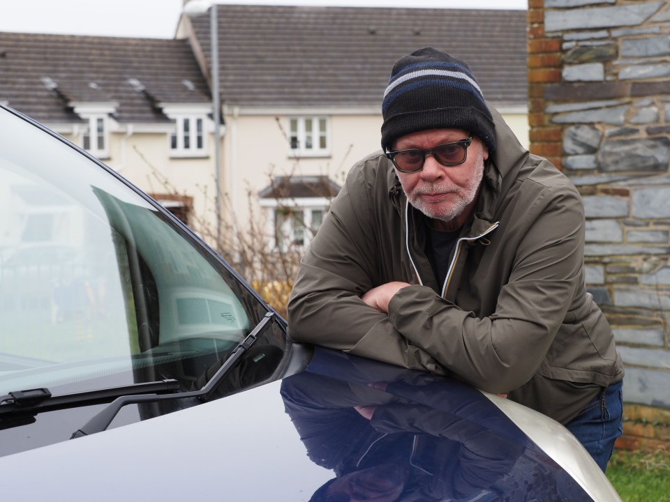 Man leaning on a car hood, looking upset.