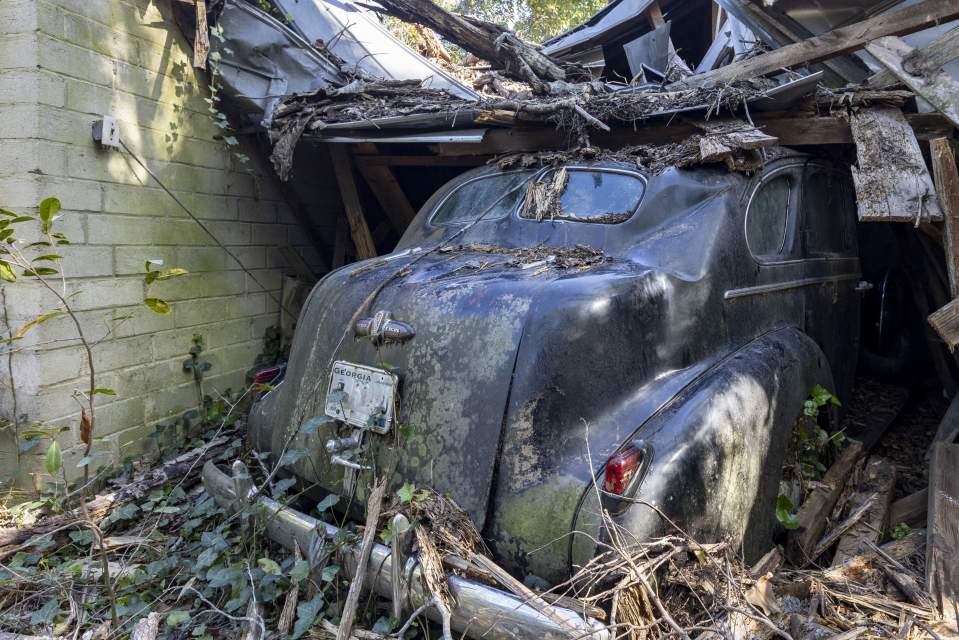 Vintage car partially buried in debris in a collapsed garage.