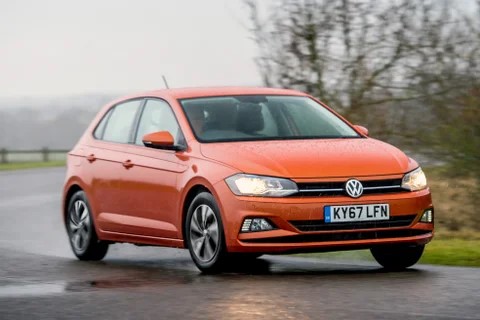 Orange Volkswagen Polo driving on a wet road.