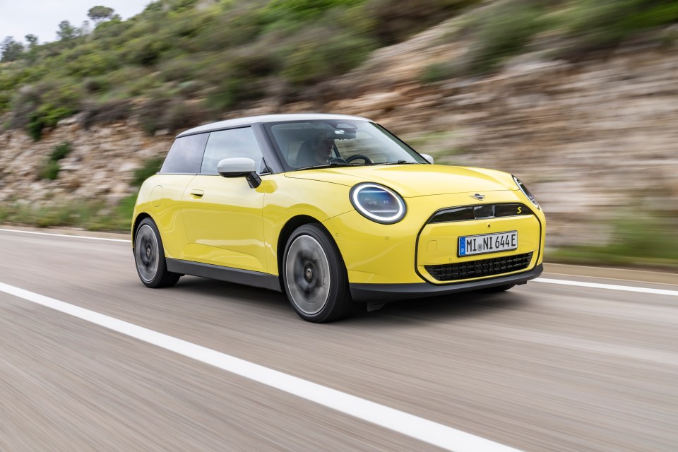 Yellow Mini Cooper driving on a road.