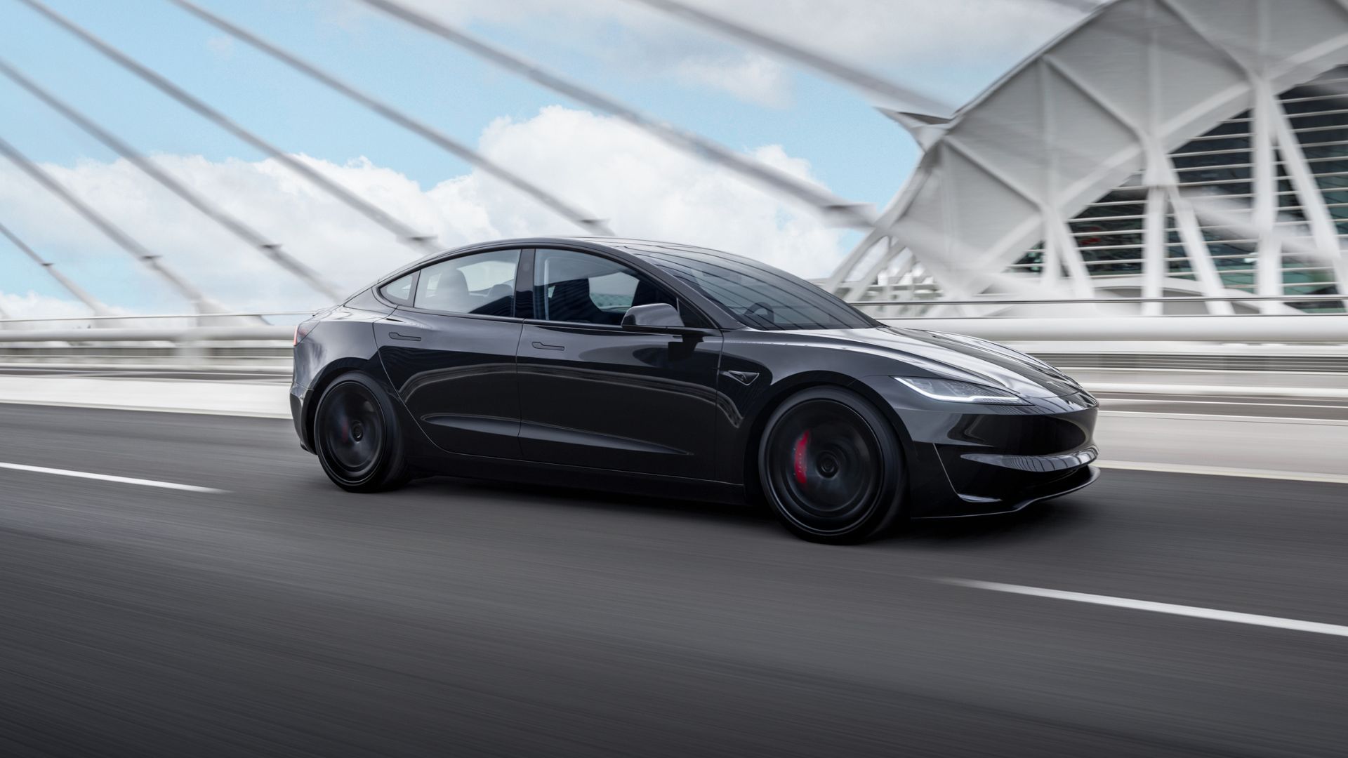 Full view of a black Tesla Model 3 Performance driving over a bridge in a city.