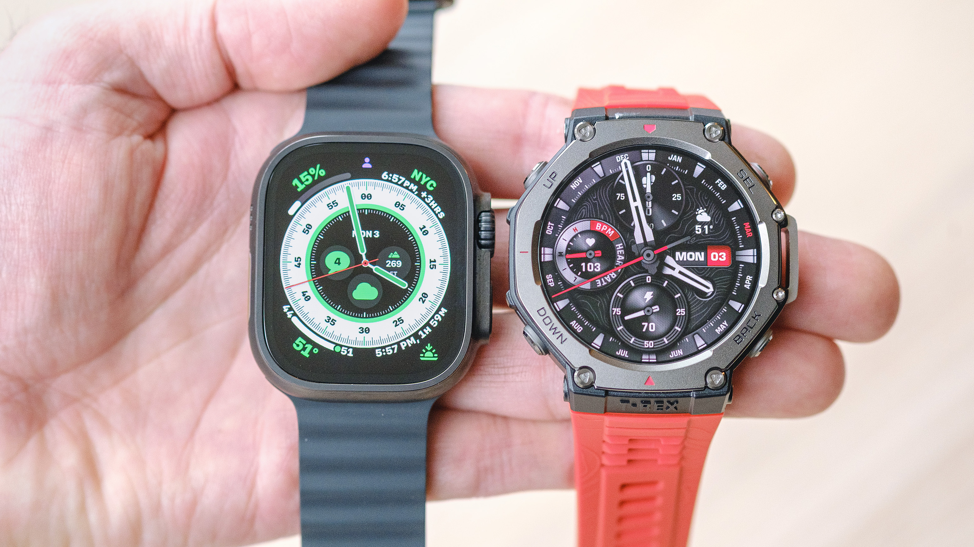 Apple Watch Ultra 2 on a black silicone strap and Amazfit T-Rex 3 on an orange silicone strap shown side-by-side in a user's hand