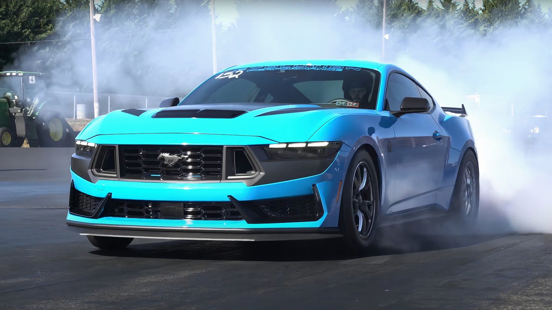 Front three-quarter view of a blue Ford Mustang Dark Horse doing burnouts